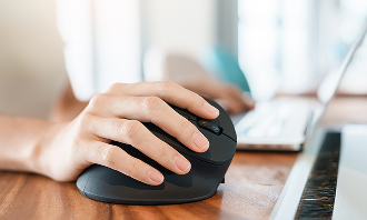 Main utilisant une souris d’ordinateur sur un bureau en bois